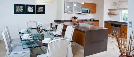 Een moderne keuken met een centraal eiland, witte kasten en een eethoek met een glazen tafel en witte stoelen.