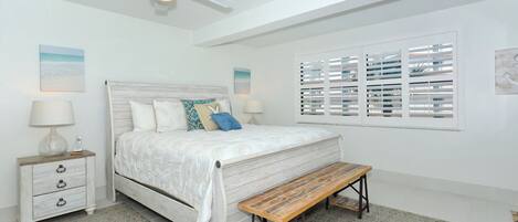 A bedroom with a bed, bedside tables, a bench, a ceiling fan, and a window with blinds.