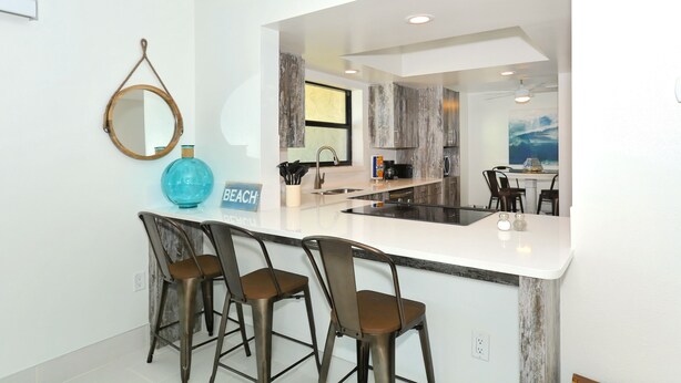 Uma cozinha moderna com área de bar, um letreiro com a inscrição "WELCOME TO THE BEACH HOUSE" e vista para a sala de jantar.