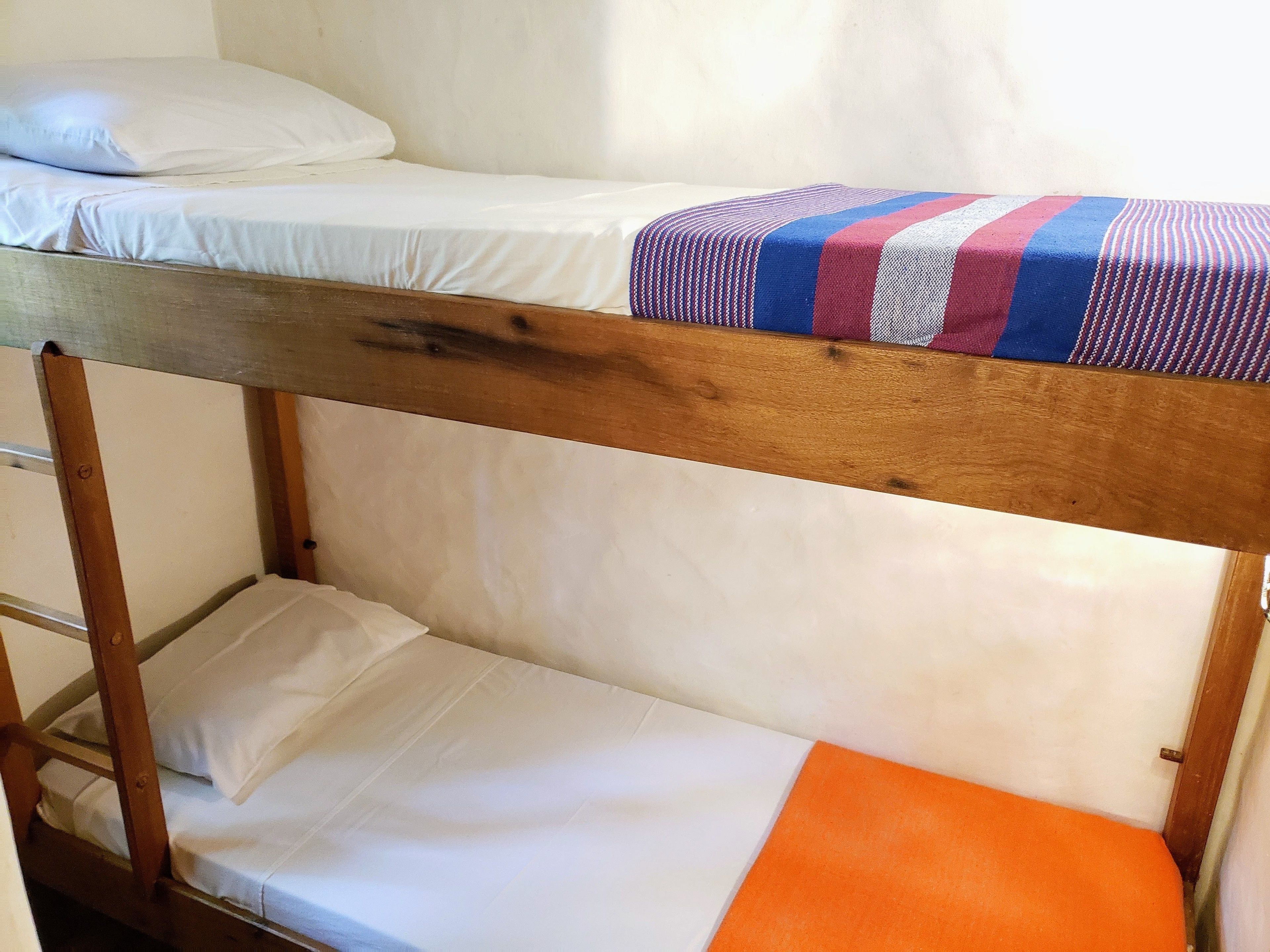 Una cama litera con estructura de madera, ropa de cama blanca y una manta a rayas en la parte superior.