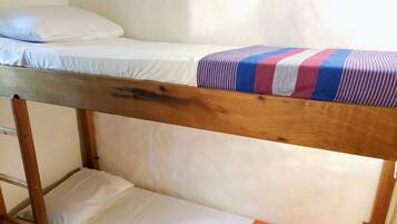 Una cama litera con estructura de madera, ropa de cama blanca y una manta a rayas en la parte superior.