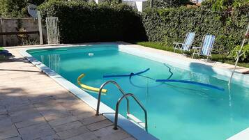 Una piscina rectangular con solárium alicatado, una escalera metálica y una tumbona.