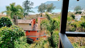 A view of a coastal area with a building surrounded by lush greenery and a clear view of the sea and mountains in the distance. - Pousada da Lagoinha (Florianópolis)