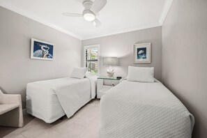 Une chambre d’hôtel avec deux lits, un ventilateur de plafond, une table de chevet avec une lampe et des œuvres d’art encadrées accrochées aux murs.