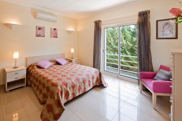 Un dormitorio con cama, mesitas de noche, cómoda, una ventana con cortinas y vistas a zonas verdes.