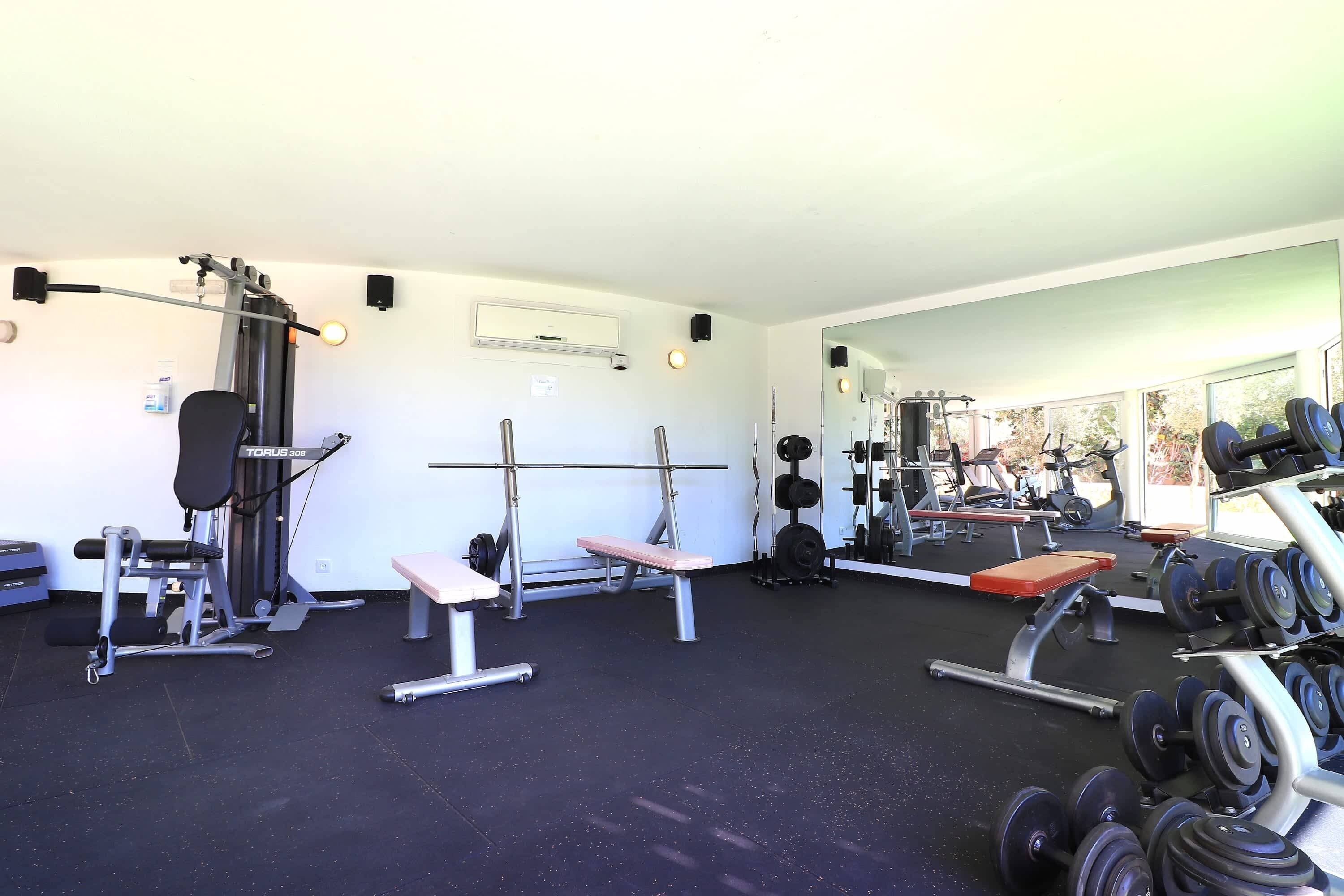 A gym with weightlifting equipment, benches, and a mirrored wall.