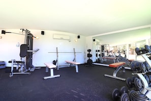 Une salle de sport équipée de matériel de musculation, de bancs et d’un mur recouvert de miroirs.