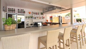 Un espace bar avec des chaises en osier, un comptoir avec une caisse enregistreuse et des étagères remplies de bouteilles et de verres.
