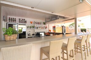 A bar area with wicker chairs, a counter with a cash register, and shelves with bottles and glasses.