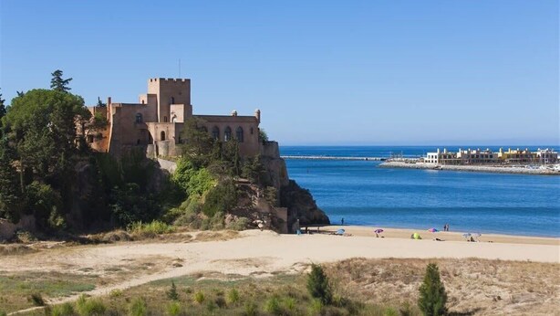 Un château situé sur la côte, avec une plage au premier plan et une jetée qui s’avance dans la mer.