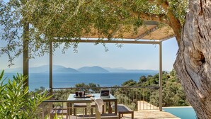 Ein Sitzbereich im Freien mit Tisch und Stühlen, mit Blick auf einen Pool und eine schöne Aussicht auf Meer und Berge.