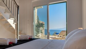 Ein Schlafzimmer mit einem großen Bett, einer Treppe und Meerblick durch eine Glastür.