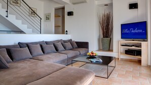 Ein modernes Wohnzimmer mit einem braunen Sofa, einem Glastisch, einem Flachbildfernseher und einer Treppe.