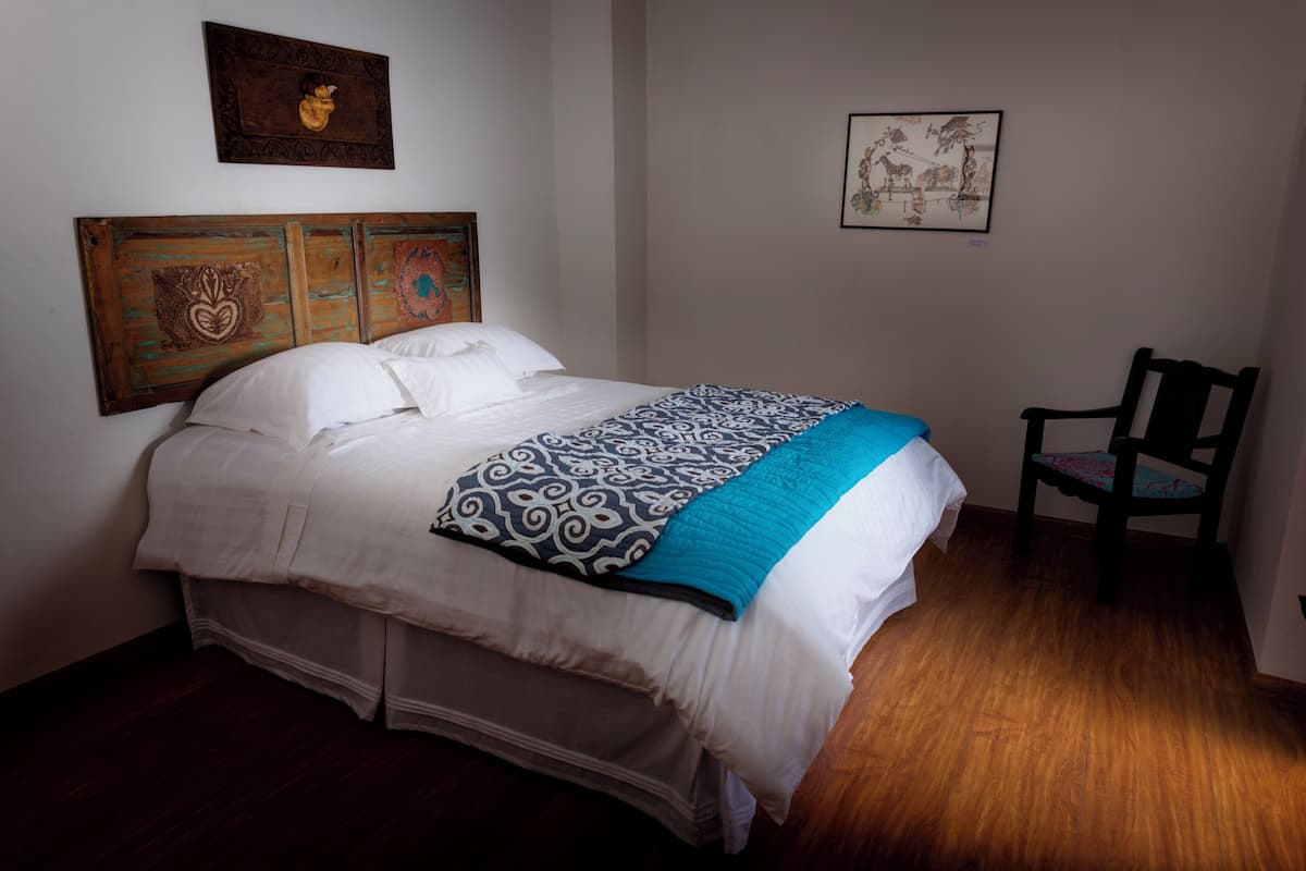 A neatly made bed with a patterned blanket, a wooden headboard, and a chair beside it.