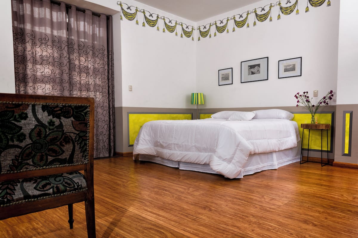 A bedroom with a bed, a chair, a bedside table, and a wall with three framed pictures.