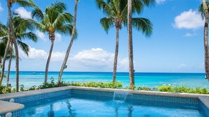A swimming pool with clear blue water, surrounded by palm trees and a view of the ocean.