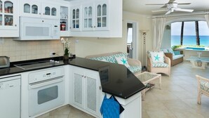 A kitchen with white cabinets, a microwave, and a built-in oven. There is a dining area with a table and chairs, and a view of the ocean.