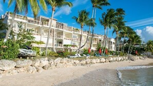 A beachfront hotel with multiple balconies, palm trees, and sun loungers.