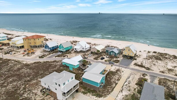 Vue aérienne d’une zone résidentielle côtière, avec des maisons situées près de la plage, un ciel dégagé et une mer calme.