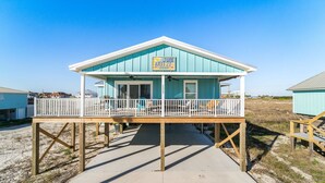 Une maison de plage dotée d’un porche couvert, d’une enseigne indiquant « June Breeze » et offrant une vue sur la plage.