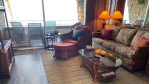 Una sala de estar con un sofá, sillones, una mesa de centro de vidrio y vistas al océano a través de grandes ventanales.
