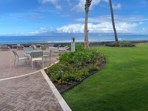 A patio with outdoor seating, a grassy area, and a view of the ocean.