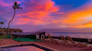 Zona junto a la piscina con sillones de descanso y vista al océano al atardecer.