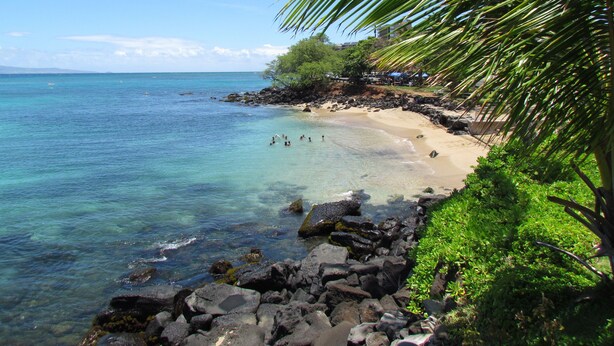 Una playa con agua turquesa cristalina, costa rocosa y vegetación exuberante.