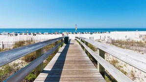 A wooden boardwalk leading to a beach with white sand and a clear blue sky.