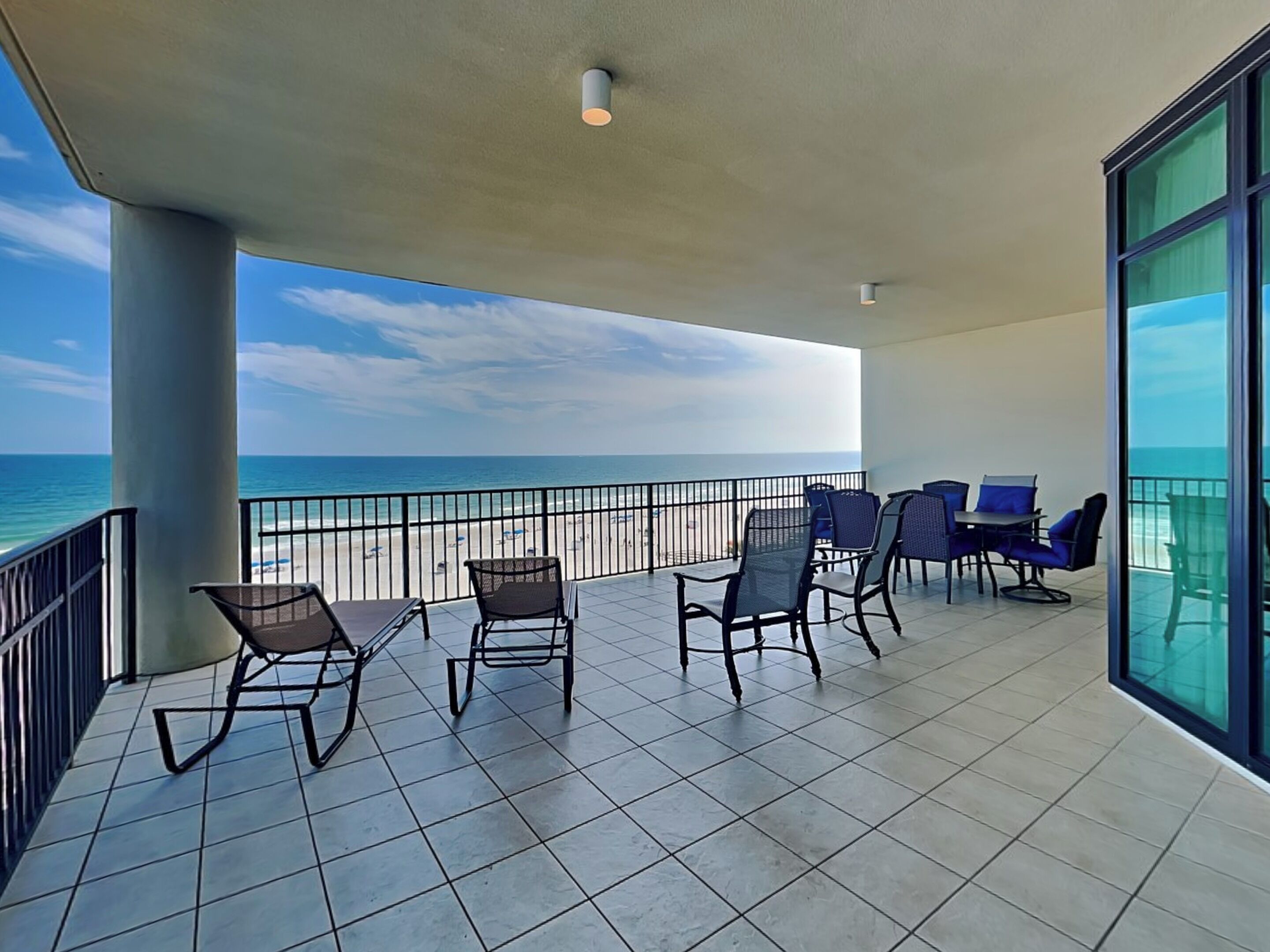 A balcony with chairs and a table, overlooking a beach and the ocean.