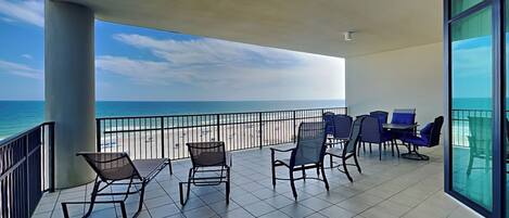 A balcony with chairs and a table, overlooking a beach and the ocean.