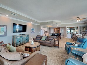 Amplia sala de estar con un televisor grande, un mueble de madera y una cocina al fondo.