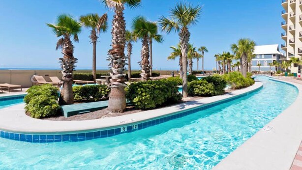 A pool area with palm trees, lounge chairs, and a view of the ocean.