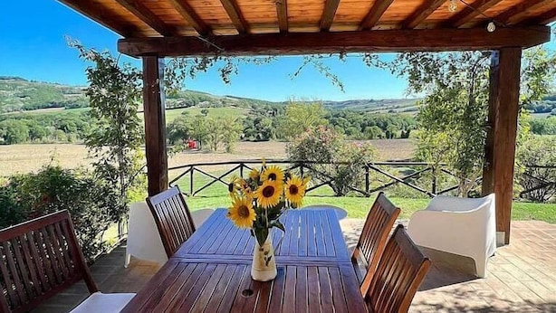 A wooden table with a vase of sunflowers, surrounded by chairs, under a pergola with a view of a hilly landscape. - Villa Gramigna: A charming two-story villa surrounded by the greenery. (Pontecuti)