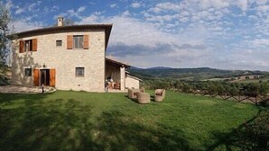 A stone house with a curved roof, a small porch, and a view of rolling hills in the background. - Villa Gramigna: A charming two-story villa surrounded by the greenery. (Pontecuti)