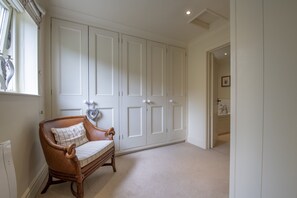 A hallway with a wooden chair, a white wardrobe, and a door leading to a bathroom.