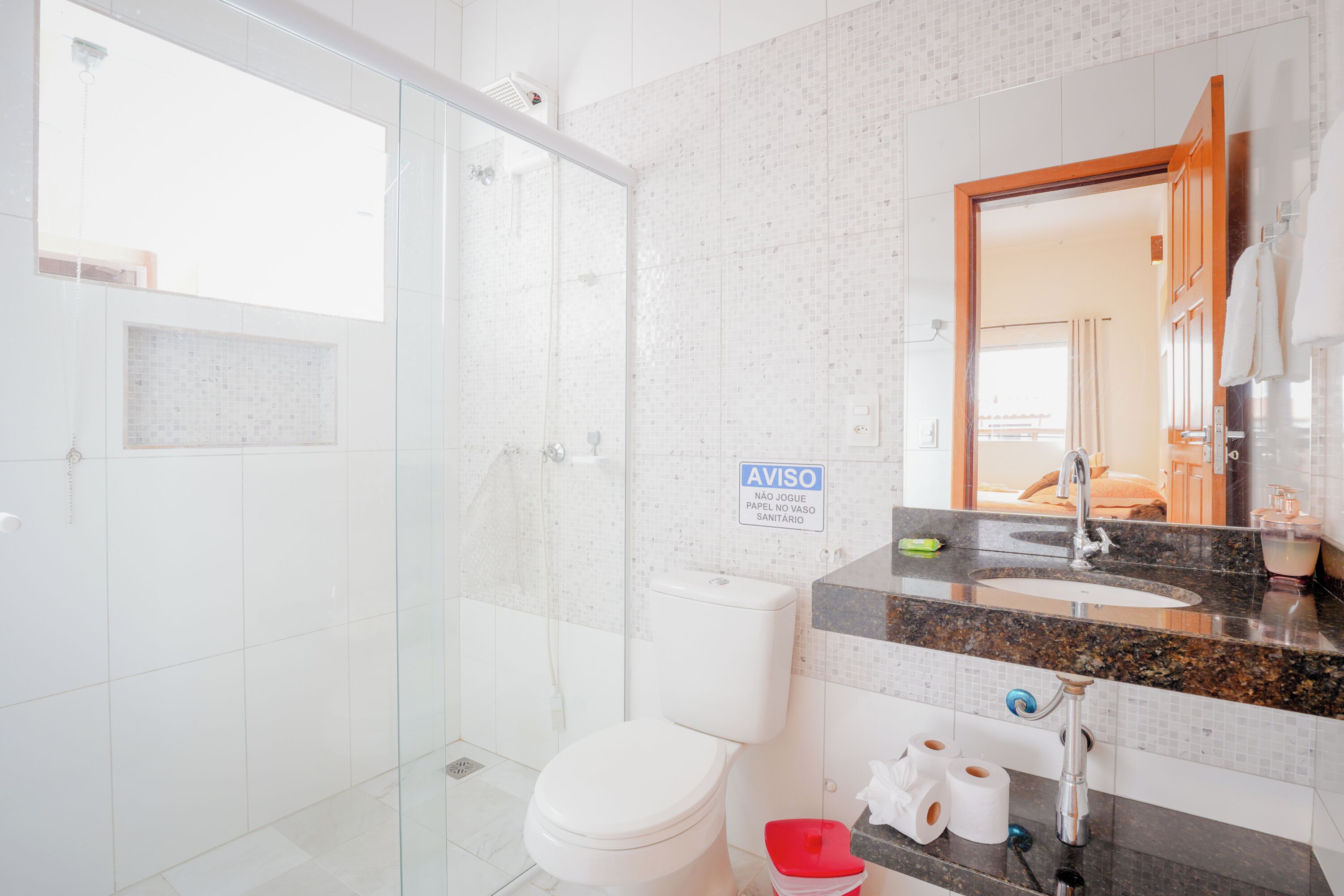 Un baño moderno con cabina de ducha de vidrio, inodoro blanco, encimera de granito y lavamanos con espejo.