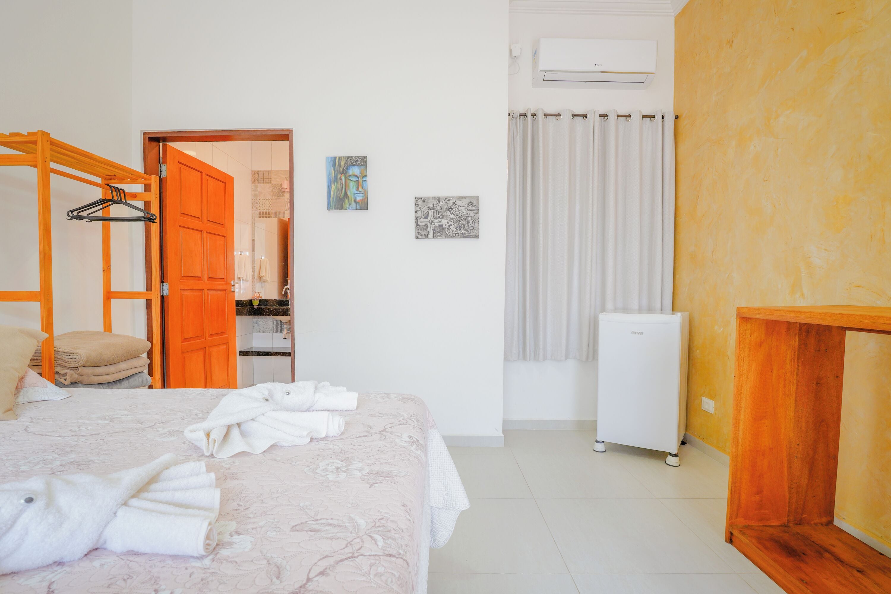 A hotel room with a bed, a wooden wardrobe, a white air conditioner, and a small table.