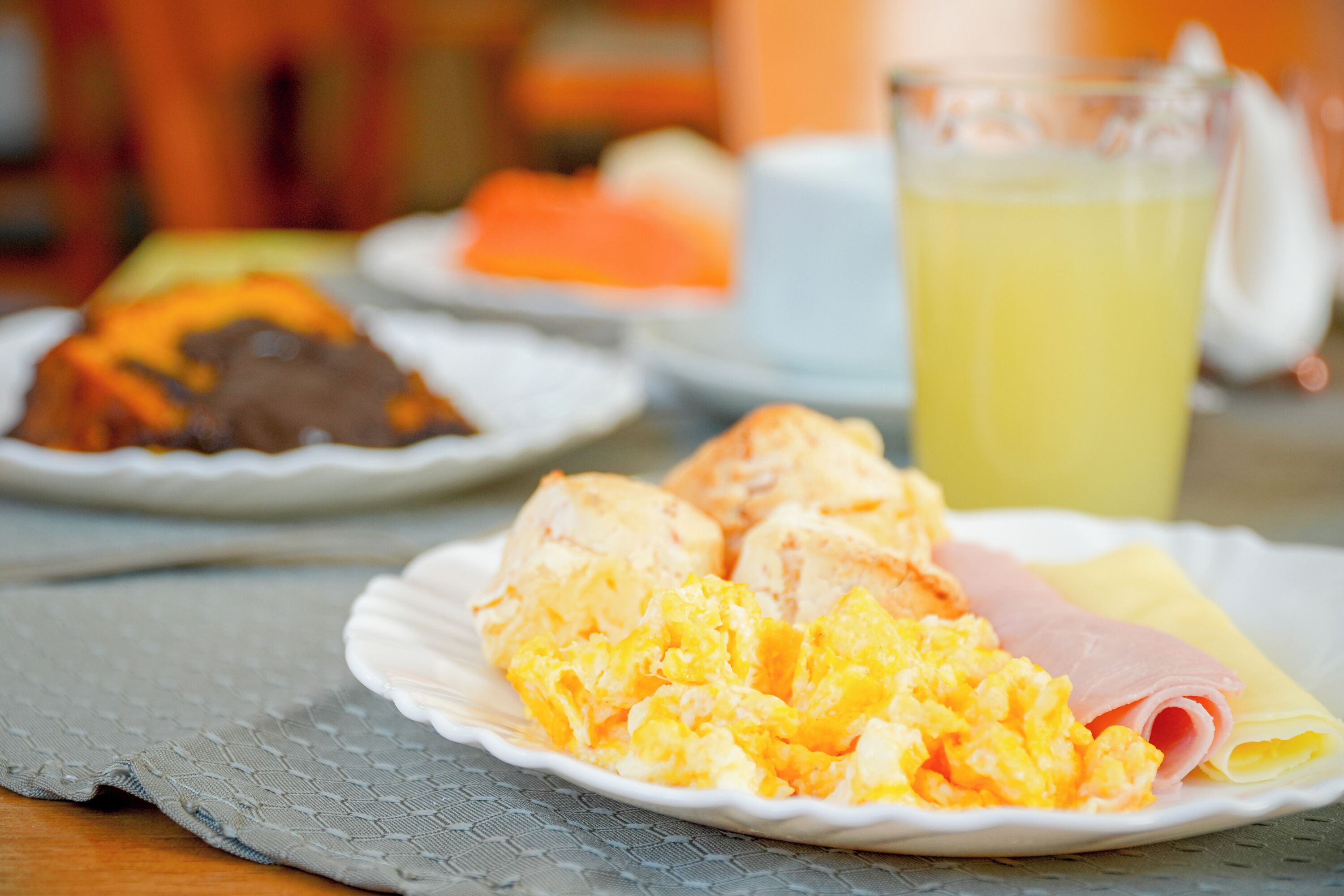 A breakfast setting with scrambled eggs, ham, and a glass of orange juice on a table.