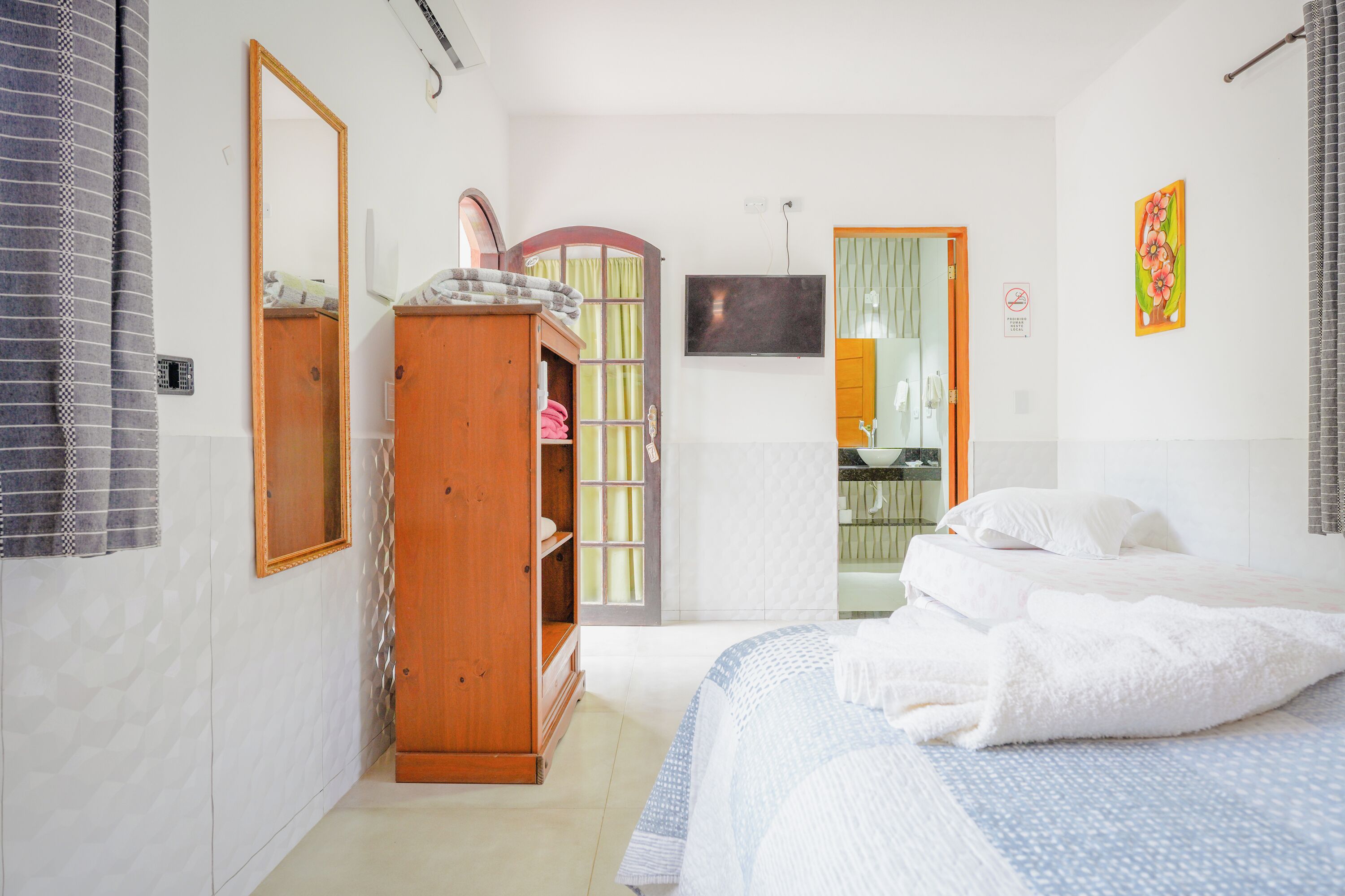 A bedroom with a bed, a wardrobe, a television, and a bathroom visible through an open door.