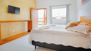 Une chambre à coucher avec un lit, un téléviseur fixé au mur et une fenêtre avec des rideaux.