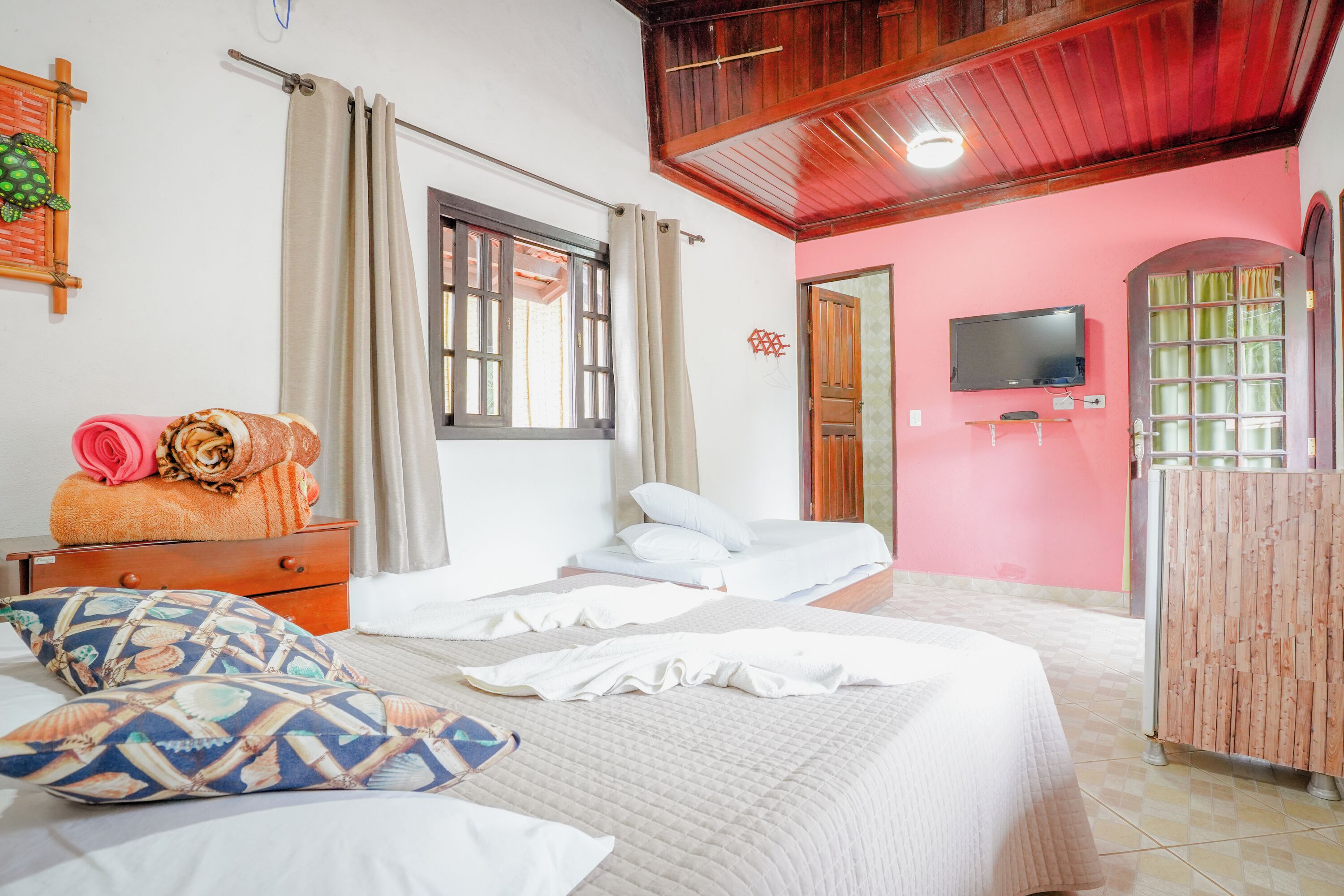 Un dormitorio con dos camas, televisión, armario de madera y ventana con cortinas.