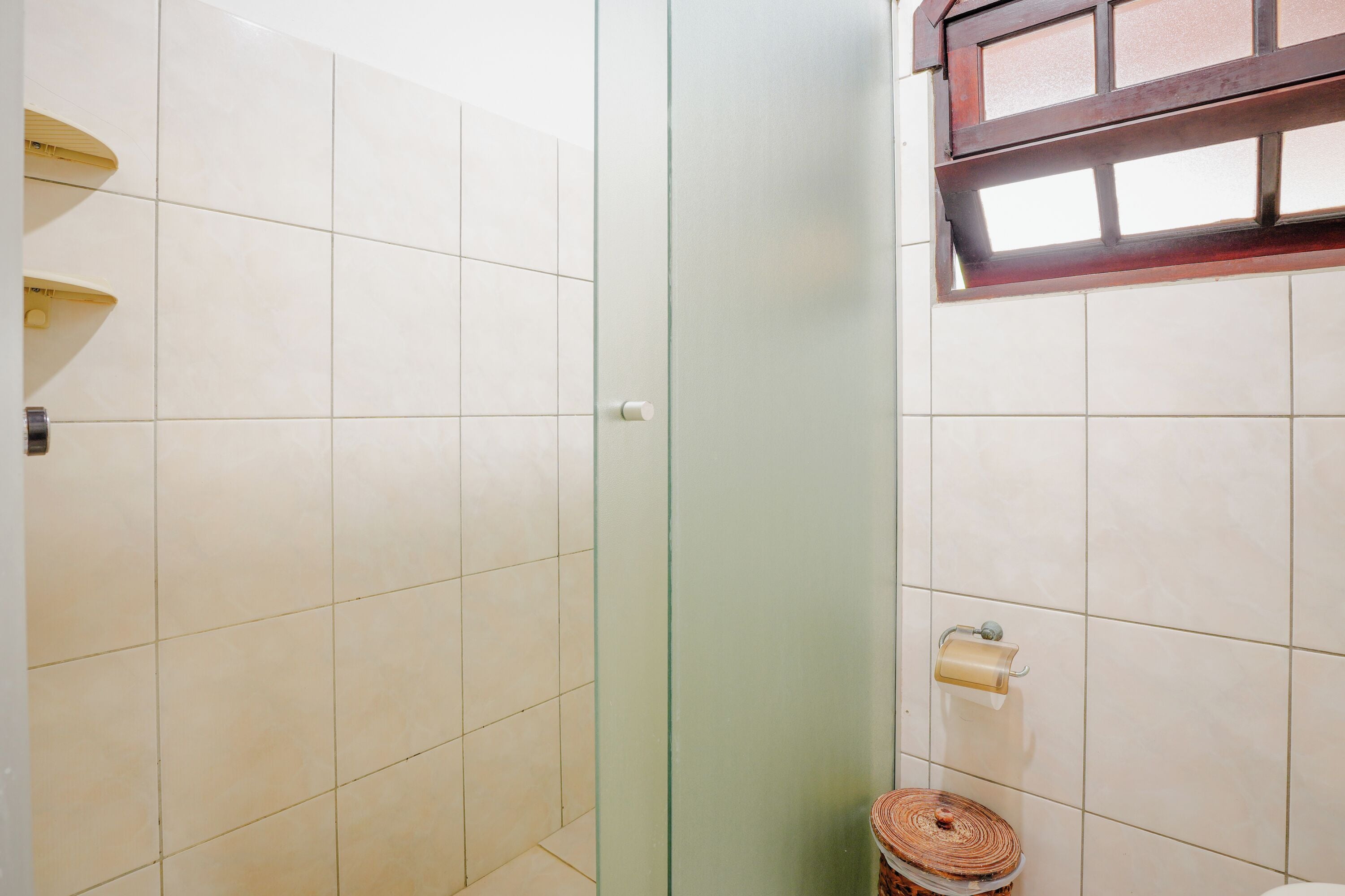 Une salle de bain avec des carreaux blancs, une douche en verre et des toilettes dotées d’un porte-serviettes en papier.