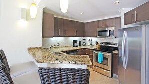 A modern kitchen with dark brown cabinets, stainless steel appliances, a granite countertop, and pendant lighting. - Modern Beachfront Condo with Pool - Sapphire 205 (Saint Lawrence Gap)