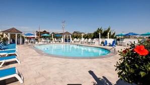 A swimming pool with lounge chairs and umbrellas, surrounded by buildings and greenery. - CR102 - Sea La Vie by First Flight Rentals (Kill Devil Hills)