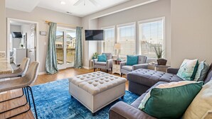 A living room with a sofa, ottoman, TV, and a ceiling fan. - CR102 - Sea La Vie by First Flight Rentals (Kill Devil Hills)