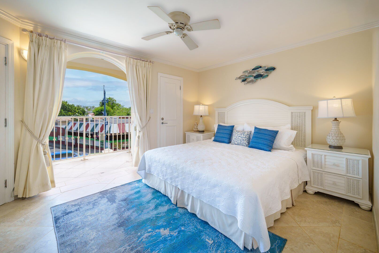Une chambre avec un grand lit, un balcon avec des rideaux, un ventilateur de plafond et une vue sur l’extérieur.