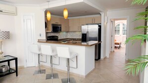 A modern kitchen with a central island, bar stools, stainless steel appliances, and pendant lighting. - Modern Beachfront Condo with Pool - Sapphire 109 (Saint Lawrence Gap)