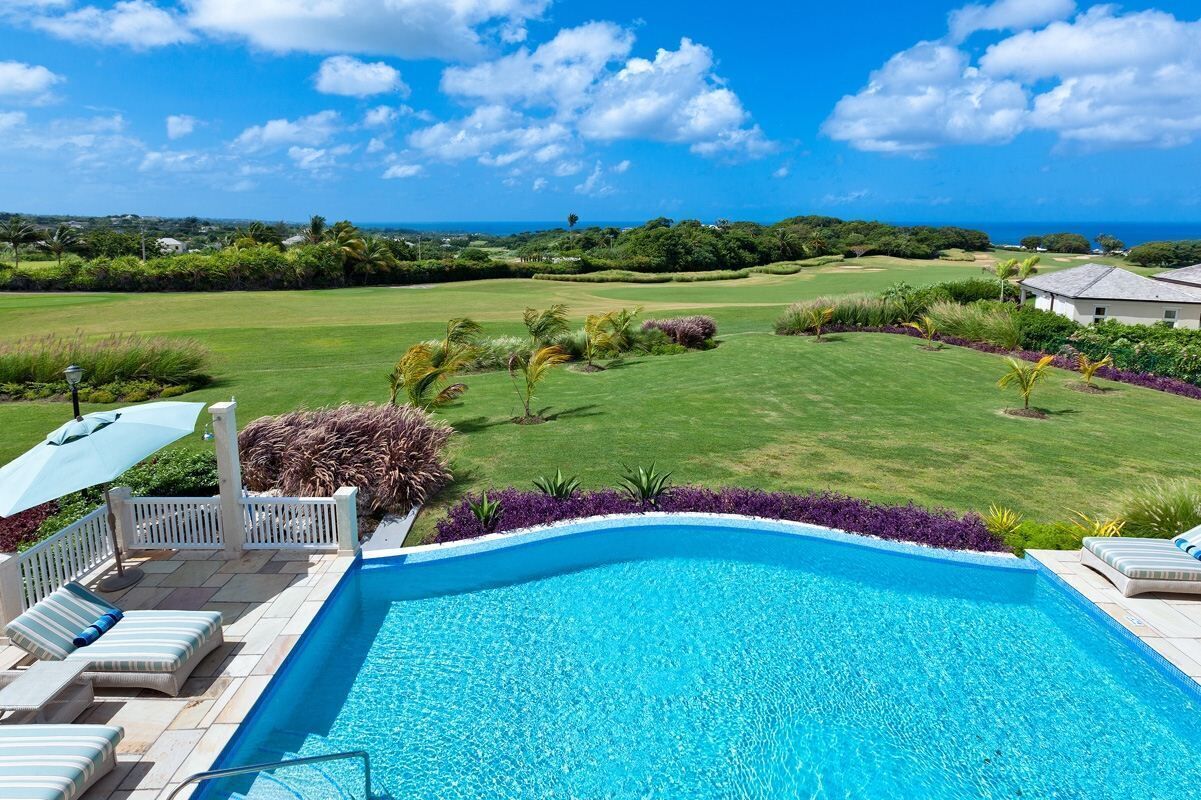 A swimming pool with lounge chairs and a view of a golf course and ocean.