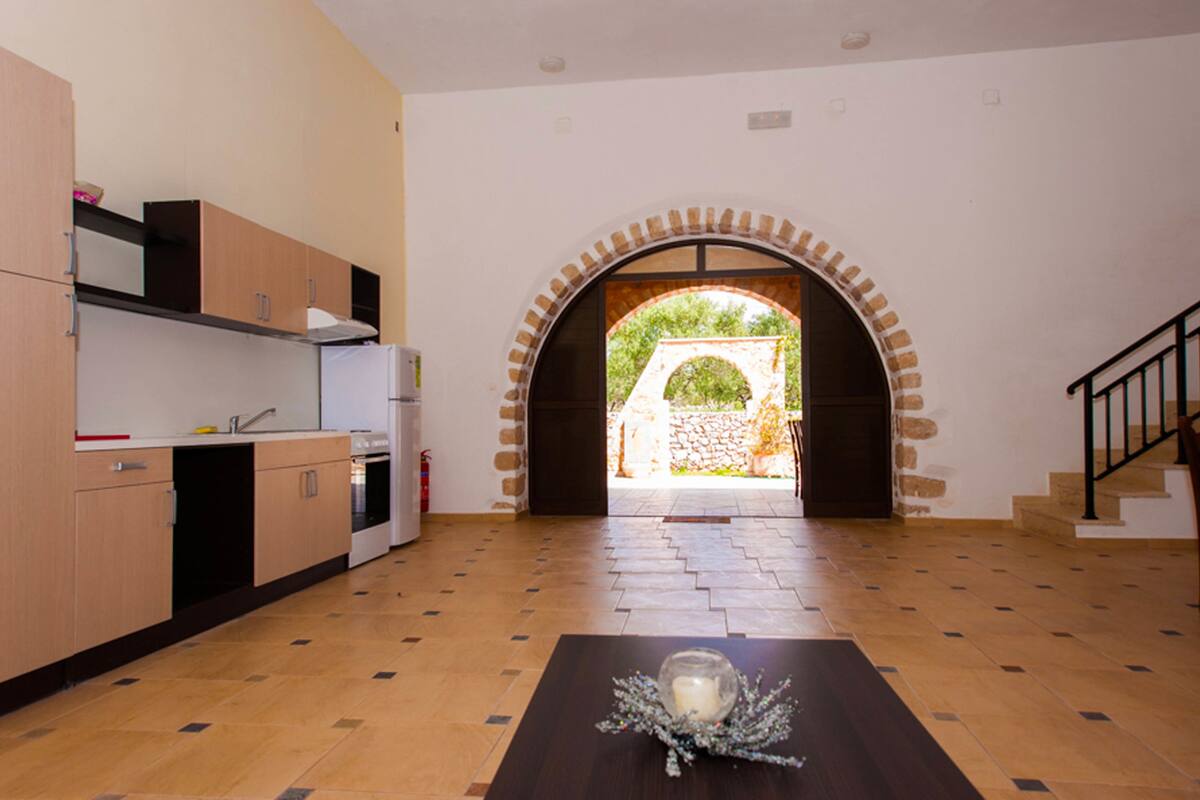 A modern kitchen with wooden cabinets, a built-in oven, and a view through an arched doorway to an outdoor area.